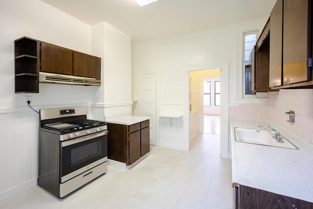 kitchen with sink, ventilation hood, dark brown cabinets, stainless steel range with gas cooktop, and backsplash