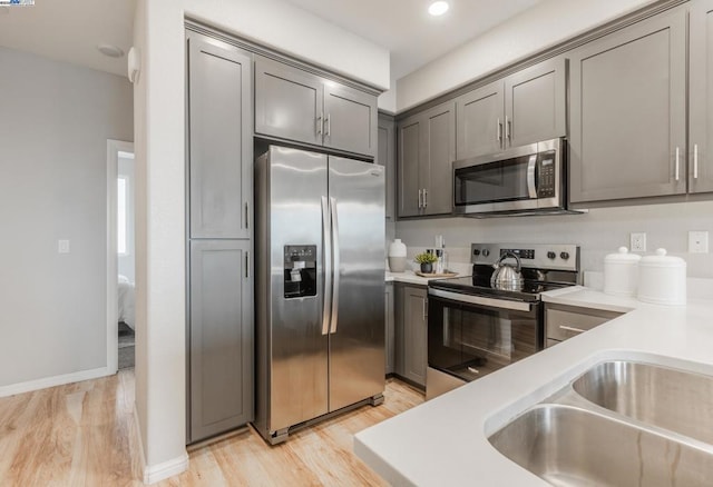 kitchen featuring appliances with stainless steel finishes, gray cabinets, sink, and light wood-type flooring