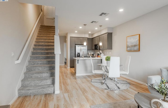 kitchen featuring gray cabinetry, hanging light fixtures, stainless steel appliances, and light wood-type flooring