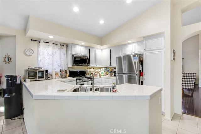 kitchen featuring light tile patterned floors, sink, appliances with stainless steel finishes, tile counters, and vaulted ceiling