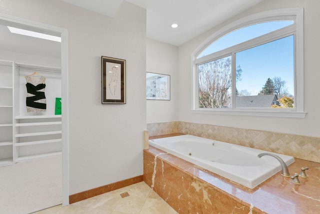 bathroom with tile patterned flooring, a relaxing tiled tub, and a skylight