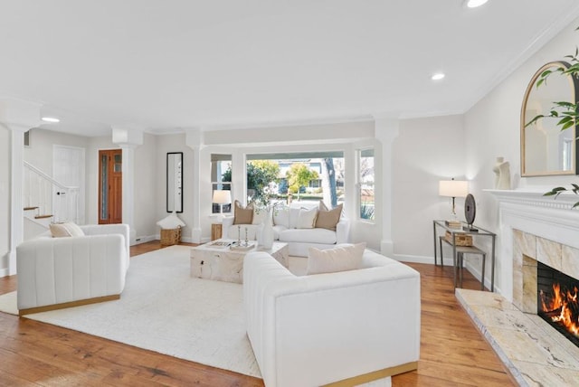 living room featuring ornamental molding, a premium fireplace, decorative columns, and light wood-type flooring