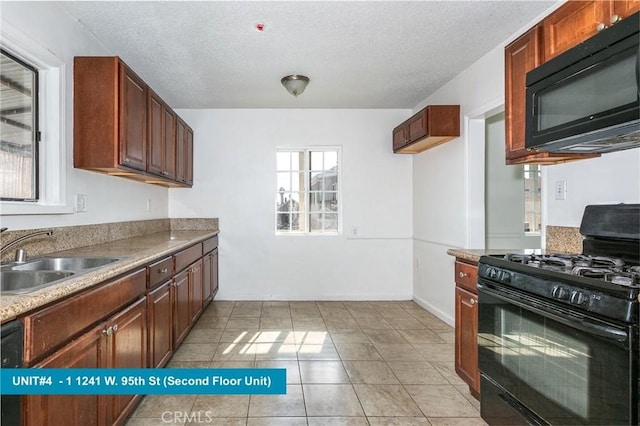 kitchen with sink, light tile patterned floors, black appliances, and a textured ceiling