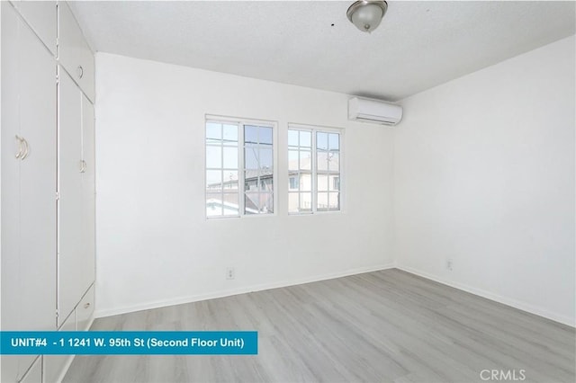 spare room with a wall mounted AC and light wood-type flooring