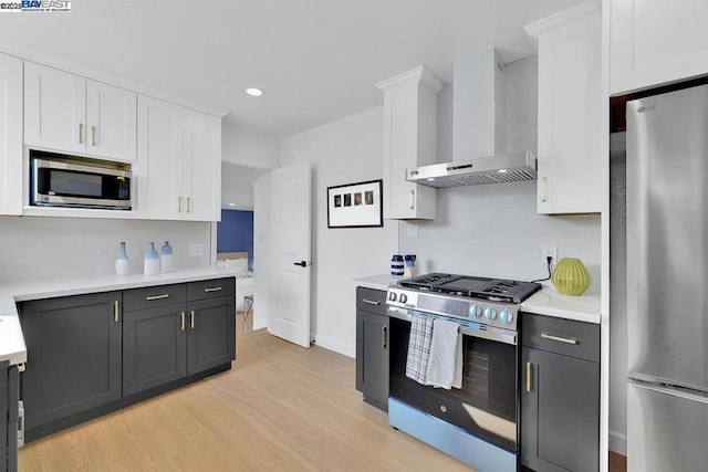 kitchen with white cabinetry, wall chimney range hood, light hardwood / wood-style flooring, and appliances with stainless steel finishes