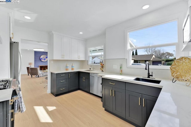 kitchen with tasteful backsplash, sink, white cabinets, stainless steel appliances, and light wood-type flooring