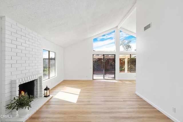 unfurnished living room with light hardwood / wood-style floors, lofted ceiling with beams, a brick fireplace, and a textured ceiling