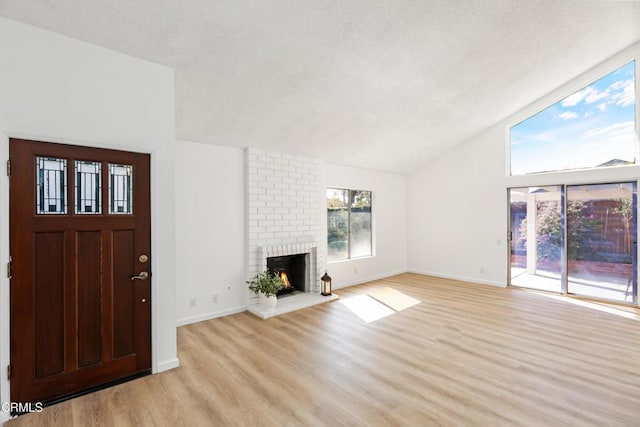 unfurnished living room with lofted ceiling, a brick fireplace, and light hardwood / wood-style flooring