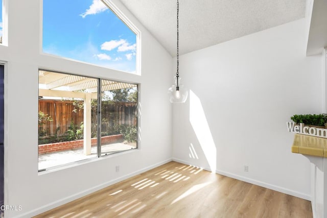 unfurnished dining area featuring hardwood / wood-style flooring, high vaulted ceiling, and a textured ceiling