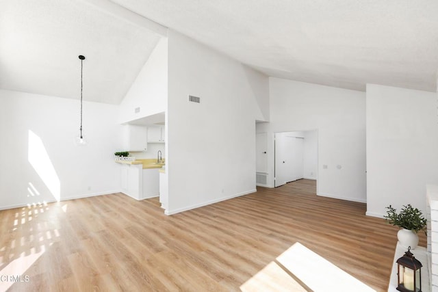 unfurnished living room with high vaulted ceiling, sink, and light hardwood / wood-style floors