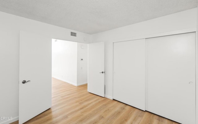 unfurnished bedroom featuring a textured ceiling, light wood-type flooring, and a closet