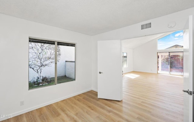 unfurnished room featuring lofted ceiling, a textured ceiling, and light wood-type flooring