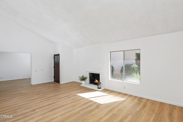 unfurnished living room with high vaulted ceiling, a brick fireplace, and light wood-type flooring