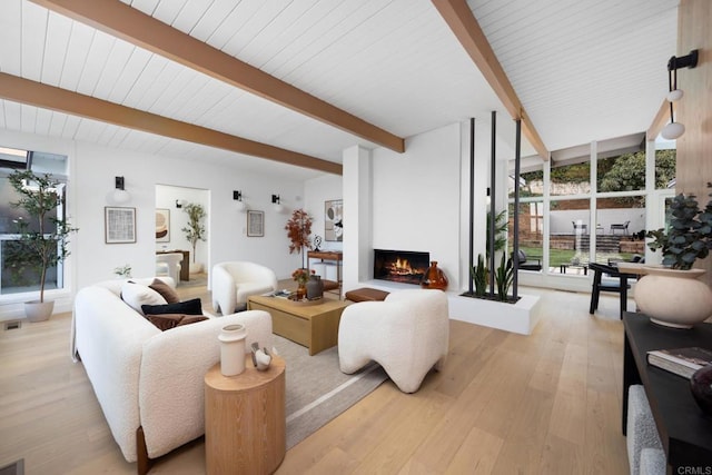 living room with beamed ceiling, expansive windows, a large fireplace, and light hardwood / wood-style flooring