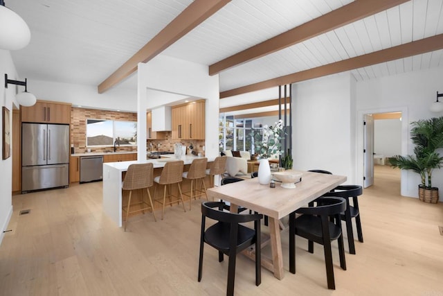 dining space featuring beamed ceiling, sink, and light hardwood / wood-style flooring