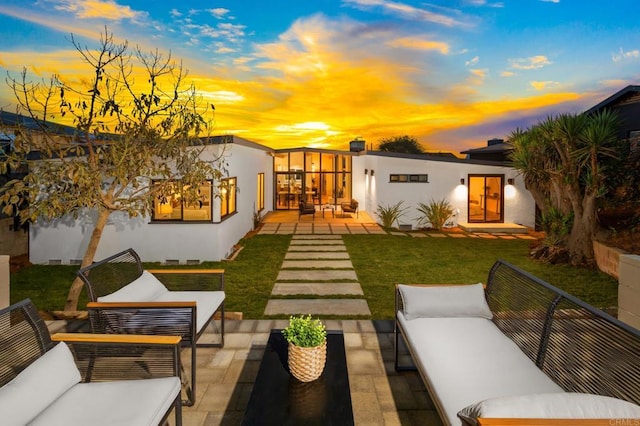 back house at dusk featuring a lawn, outdoor lounge area, and a patio