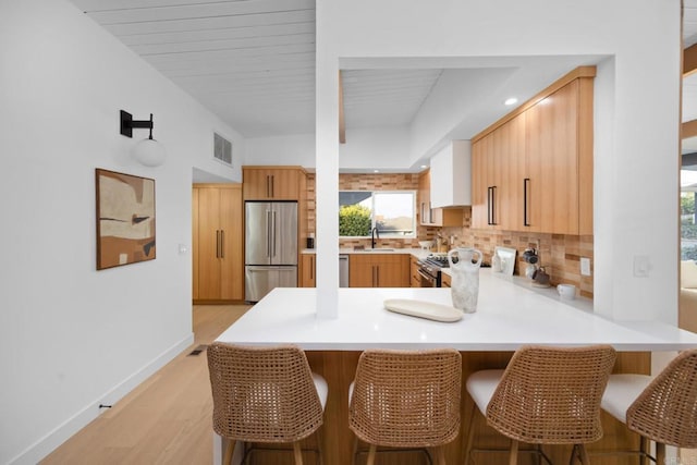 kitchen with sink, light hardwood / wood-style flooring, stainless steel fridge, backsplash, and kitchen peninsula