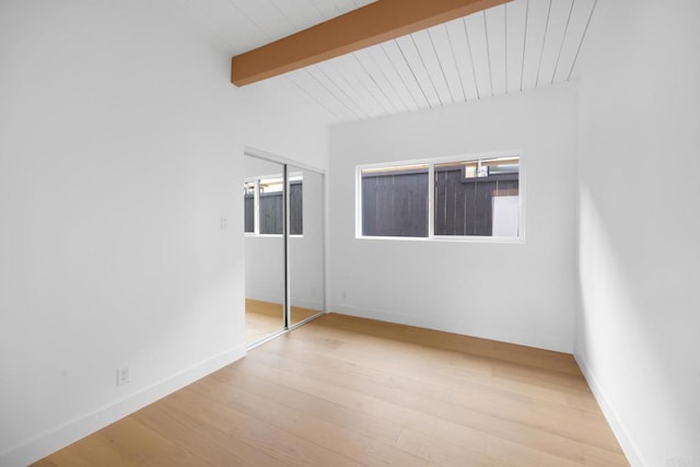 unfurnished bedroom with multiple windows, lofted ceiling with beams, a closet, and light wood-type flooring