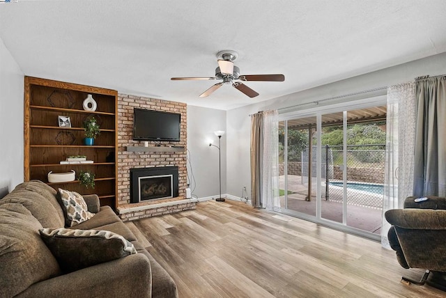 living room featuring a brick fireplace, built in features, ceiling fan, and light hardwood / wood-style flooring