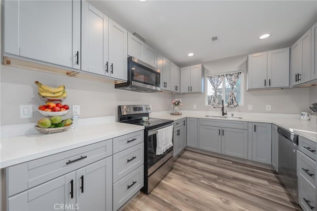 kitchen featuring gray cabinetry, sink, stainless steel appliances, and light wood-type flooring