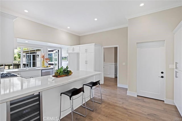 kitchen with light wood-type flooring, ornamental molding, kitchen peninsula, beverage cooler, and white cabinets