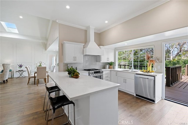 kitchen with a breakfast bar, custom exhaust hood, appliances with stainless steel finishes, kitchen peninsula, and white cabinets