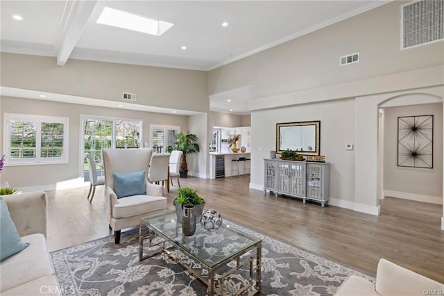 living room with wood-type flooring, a skylight, high vaulted ceiling, ornamental molding, and beam ceiling