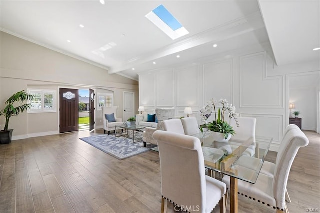 dining area featuring light hardwood / wood-style flooring, ornamental molding, and vaulted ceiling with skylight