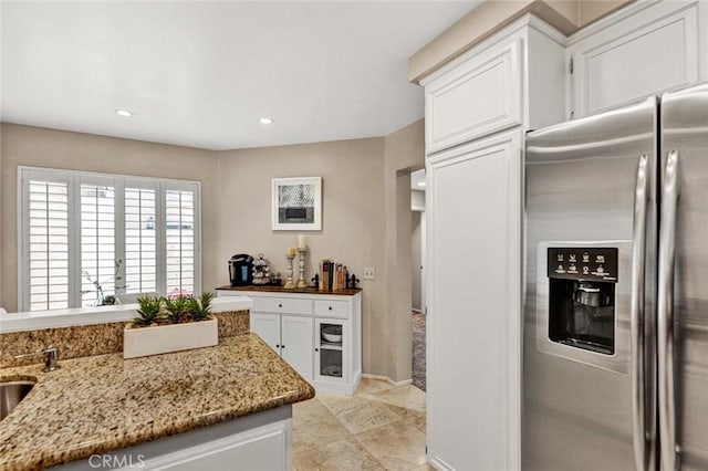 kitchen with white cabinetry, stainless steel fridge, and light stone counters