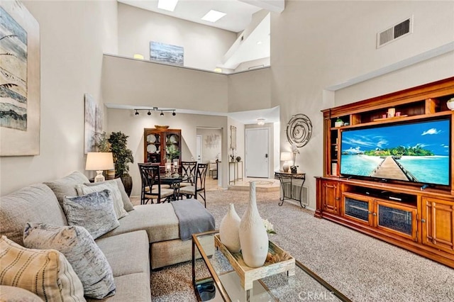 carpeted living room with a towering ceiling, rail lighting, and a skylight