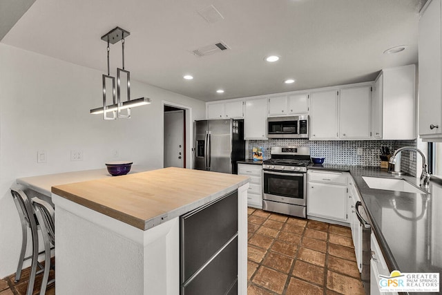 kitchen with decorative light fixtures, white cabinetry, sink, decorative backsplash, and stainless steel appliances