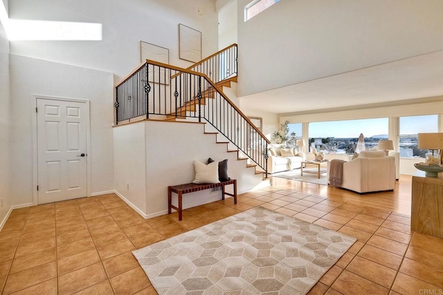 tiled entryway with baseboards, a towering ceiling, and stairs