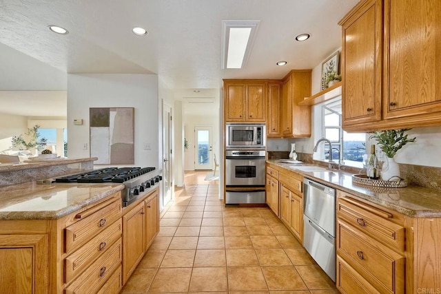 kitchen with a warming drawer, light stone counters, a sink, appliances with stainless steel finishes, and light tile patterned floors