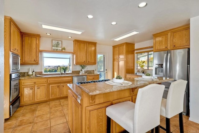 kitchen with a breakfast bar, a sink, light stone counters, a center island, and appliances with stainless steel finishes