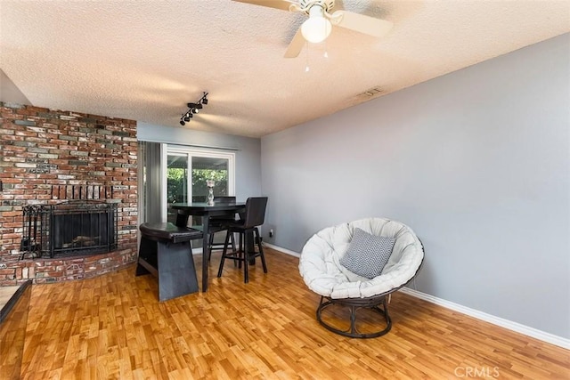 interior space featuring ceiling fan, a brick fireplace, light hardwood / wood-style floors, and a textured ceiling