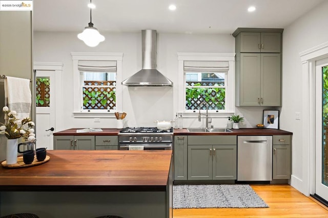 kitchen featuring wood counters, sink, light wood-type flooring, stainless steel appliances, and wall chimney range hood