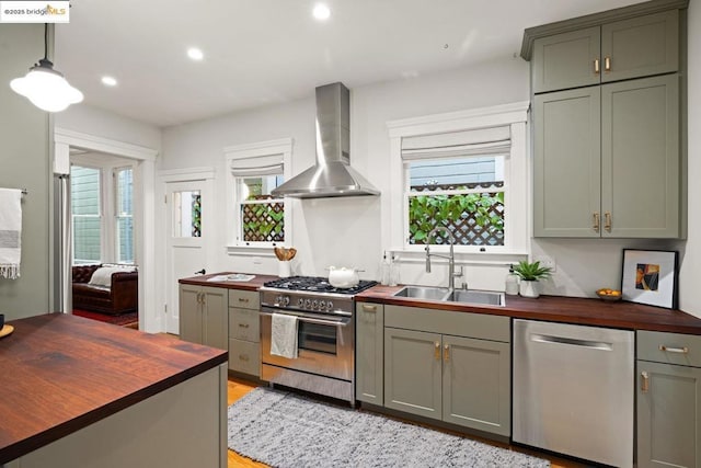 kitchen with stainless steel appliances, sink, butcher block counters, and wall chimney range hood