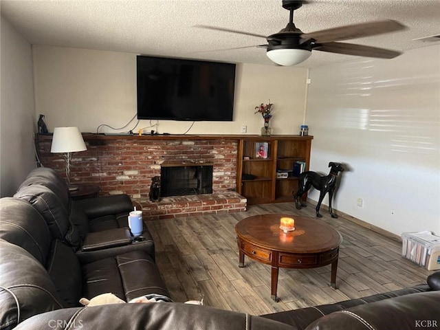 living room featuring ceiling fan, a brick fireplace, hardwood / wood-style floors, and a textured ceiling