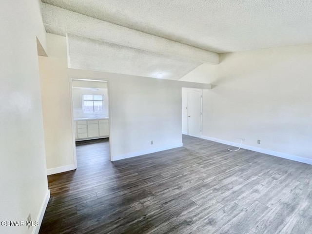 unfurnished room with dark hardwood / wood-style floors, a textured ceiling, and vaulted ceiling with beams