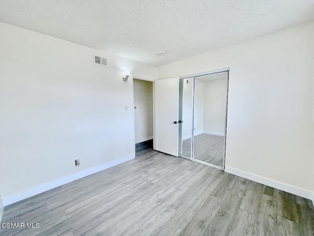 unfurnished bedroom featuring a closet, a textured ceiling, and light hardwood / wood-style flooring