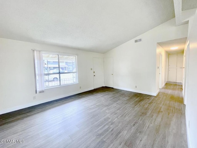 unfurnished room featuring lofted ceiling, a textured ceiling, and light hardwood / wood-style flooring