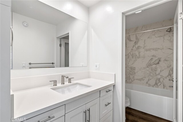 full bathroom with tiled shower / bath combo, wood-type flooring, vanity, and toilet