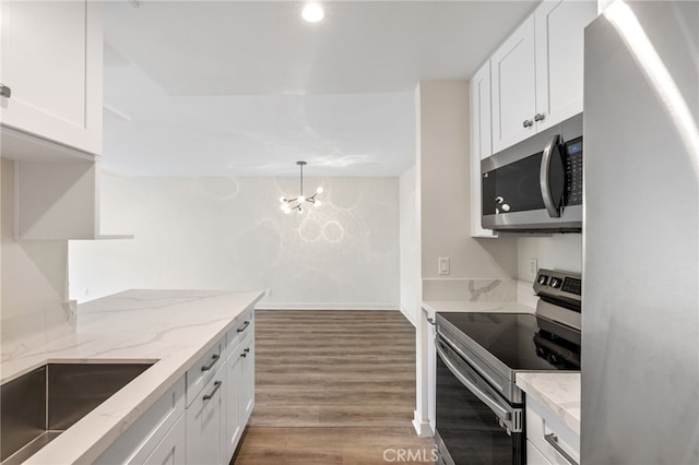 kitchen with appliances with stainless steel finishes, hanging light fixtures, light stone counters, light hardwood / wood-style floors, and white cabinets