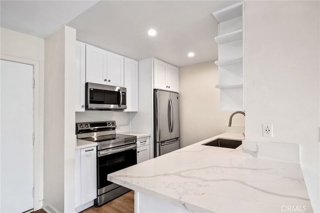 kitchen with sink, white cabinets, stainless steel appliances, light stone countertops, and light hardwood / wood-style flooring