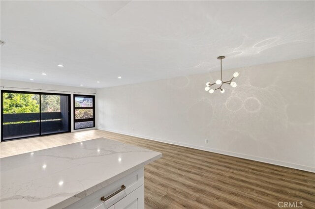 kitchen featuring hardwood / wood-style floors, white cabinets, hanging light fixtures, a notable chandelier, and light stone counters