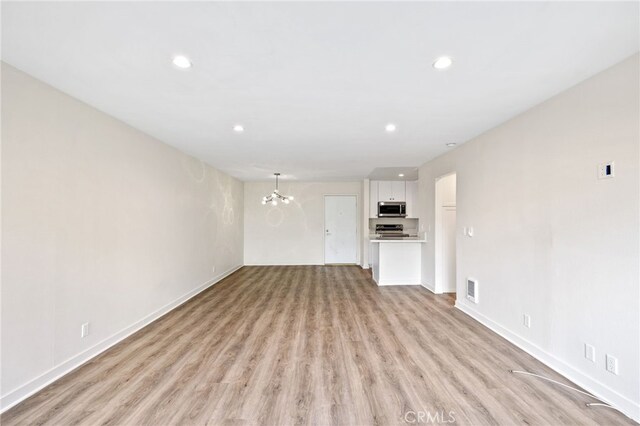 unfurnished living room with an inviting chandelier and light hardwood / wood-style flooring