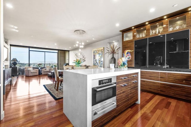 kitchen with dark hardwood / wood-style floors, floor to ceiling windows, stainless steel oven, and a kitchen island