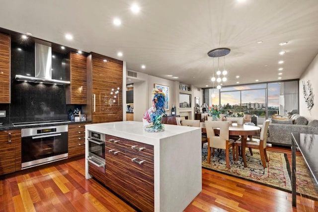 kitchen featuring wall chimney exhaust hood, stovetop, a center island, light hardwood / wood-style flooring, and oven