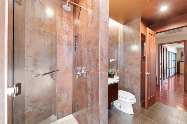 bathroom with tile walls, vanity, toilet, a shower with door, and tile patterned floors