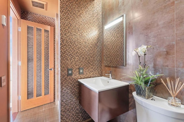 bathroom with vanity, toilet, tile patterned flooring, and tile walls